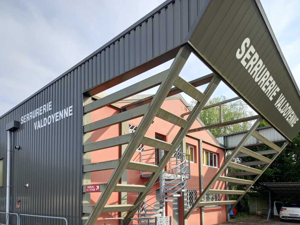 Homme d'affaires souriant utilisant un téléphone portable et un ordinateur portable dans un espace de travail industriel moderne