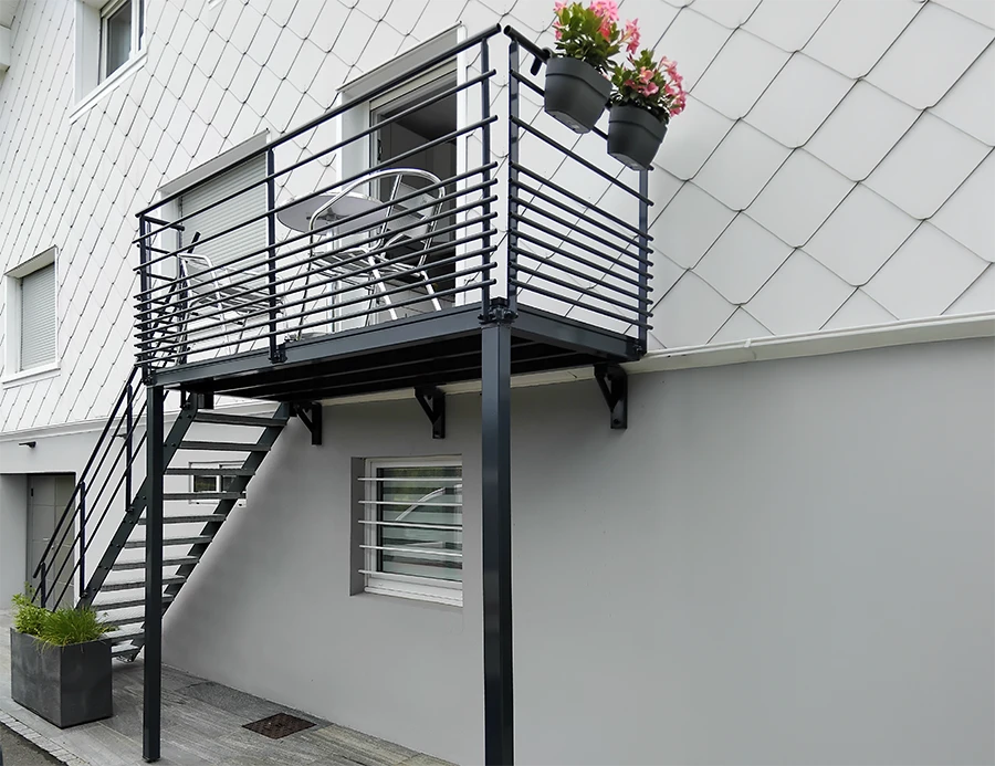 Escalier extérieur métallique avec marches en caillebotis noir fixé sur façade blanche